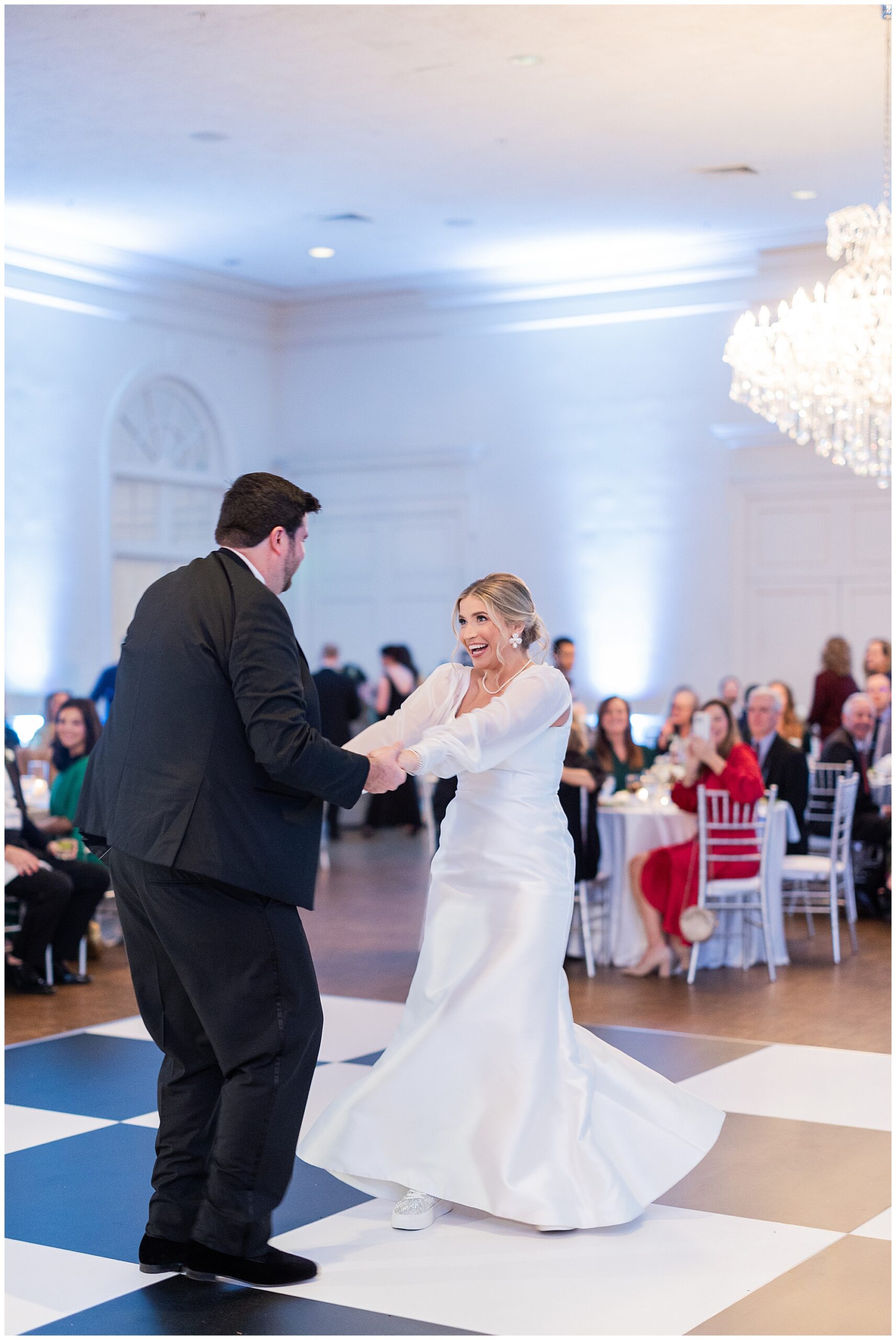 Faith and James share their first dance in the middle of the room on a black and white checkered dance floor, surrounded by their guests. 